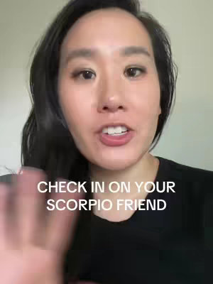 A woman with long black hair is centered in the frame, smiling and holding up her hand. Text overlayed on the image reads, 'CHECK IN ON YOUR SCORPIO FRIEND' in white text.