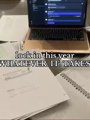 The image shows a laptop open on a desk littered with papers and a notebook. The overlay text says 'lock in this year / WHATEVER. IT. TAKES.'