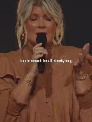 A medium shot shows a woman with blonde hair wearing a brown top, holding a black microphone and singing. Text overlayed on the image reads, “I could search for all eternity long”.