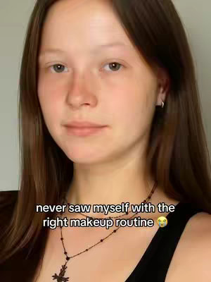 A close-up shot of a young woman's face looking directly at the camera. She has long, dark brown hair and is wearing a black top and a delicate necklace. The background is a simple, light-colored wall. The lower half of a text overlay is partially visible across the bottom of the image.