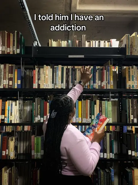 A person, viewed from behind, reaches for a book on a shelf within a library setting, conveying a sense of curiosity and the joy of reading. The image is dominated by a vast library with numerous books lining the shelves.