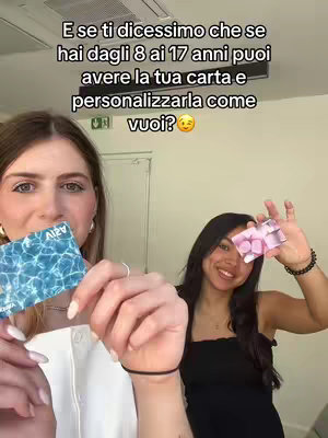Two young women are holding up credit/debit cards in front of them. The text is overlaid at the top of the image. One woman is on the left, holding a light-blue card while the other is on the right, holding a pink card. The subjects are in front of a plain white wall.