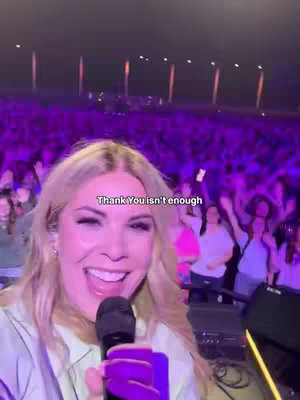 The cover image shows a woman with blonde hair smiling and holding a microphone, appearing to sing on stage. Behind her, a large crowd with their hands in the air adds depth to the scene. Text overlayed on her shows "Thank You isn't enough". The background is lit with purple lights.