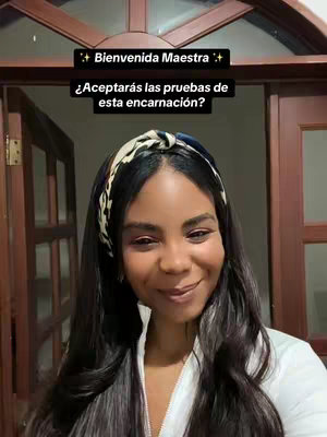A woman with long, dark wavy hair is smiling. She is wearing a white top and a headband. The background is a doorway and interior walls. The image has overlaid text.