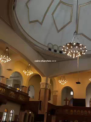 The image features the interior of a church with a high, arched ceiling and decorative chandeliers. The lighting is warm, and the overall composition is symmetrical, emphasizing the architectural details.