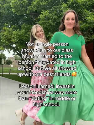Two young women stand side-by-side in an outdoor setting with lush green foliage in the background. The woman on the left is blonde and wearing a pink floral dress, while the woman on the right has brown hair and is dressed in a green top and skirt. Text overlays are present, conveying a message about friendship.