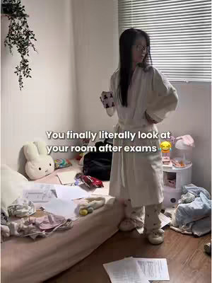 A person in a white robe stands in a messy bedroom, holding a cup, looking at the camera with a surprised expression. The bed is unmade with papers scattered around. Text on the image reads, "You finally literally look at your room after exams".
