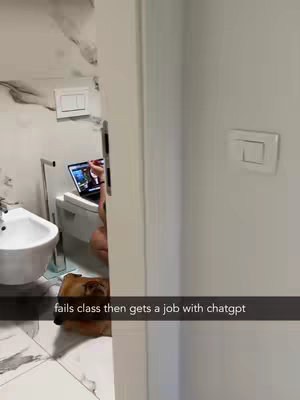 The image shows a bathroom partially visible, viewed through a doorway. On the left is a toilet with a person sitting on it, using a laptop. A dog is lying on the floor in front of the toilet. The door frame separates the different elements of the shot.