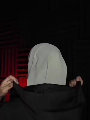 The cover image shows a person from the back, wearing a black hoodie. A white head covering obscures the person's face, which is not visible. The background is black with red, grid-like patterns.