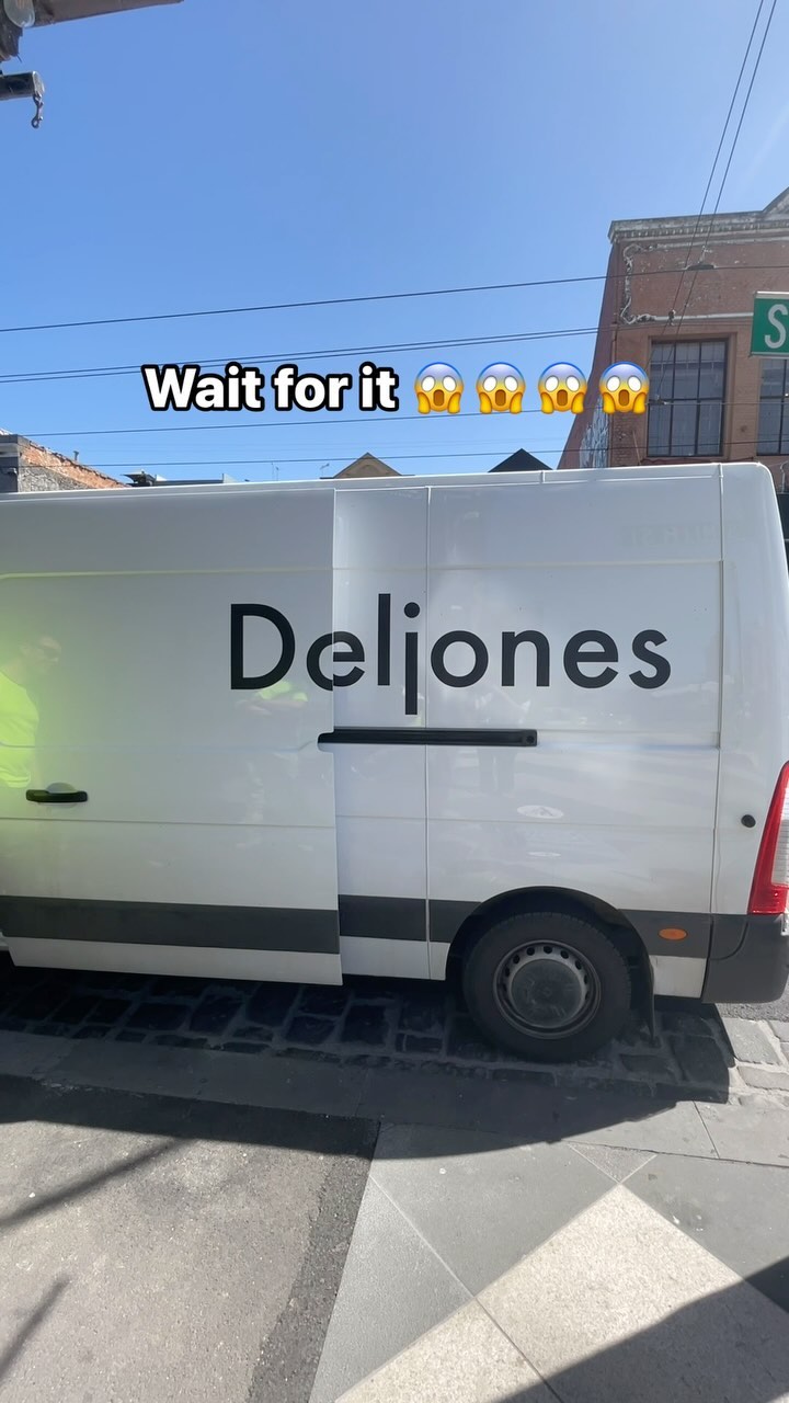 A daytime shot of a white van parked on a city street. The van has 'Deljones' written in large, bold black letters on its side. Above the van, overlaid text reads 'Wait for it' followed by three shocked face emojis. The sky is bright blue.
