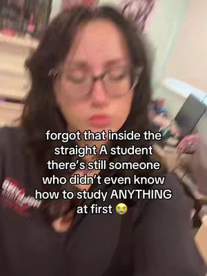 The image is a selfie-style shot featuring a young woman with dark hair and glasses. She is centered, with a slightly unfocused background hinting at an indoor setting. The text overlayed on the image reads, 'forgot that inside the straight A student there's still someone who didn't even know how to study ANYTHING at first' with a crying emoji. The overall color palette is muted, possibly due to the indoor lighting. The composition is straightforward capturing a moment of relatability.