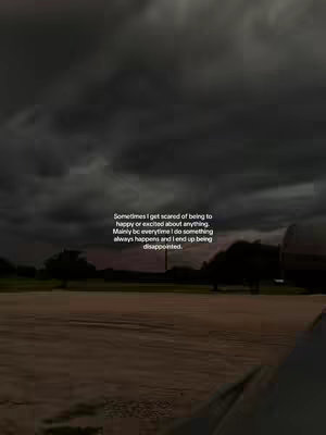 A dark, moody scene. The image is dominated by a stormy, overcast sky that takes up most of the frame. Below, a flat landscape stretches toward the horizon, with silhouetted trees or bushes visible. The ground appears to be a field. A block of white text is overlaid in the lower right, while smaller text appears to tell a story.