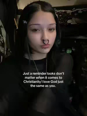 A close-up shot of a young woman with dark hair and multiple facial piercings. She is looking towards the camera with a neutral expression. Text overlayed against the background reads "Just a reminder looks don't matter when it comes to Christianity I love God just the same as you."