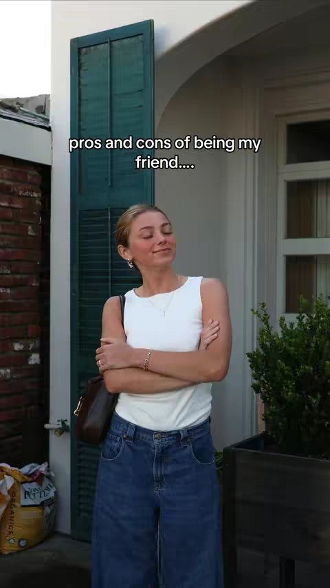 A woman stands outside near a brick wall and a green door. The text 'pros and cons of being my friend...' is overlaid on the image.