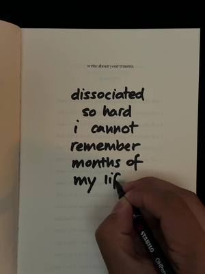 A close-up shot of a hand writing with a black pen on a page of a book, with text from the image overlayed on the book page, the book is open and the pages are light-colored. The text is handwritten in black marker.
