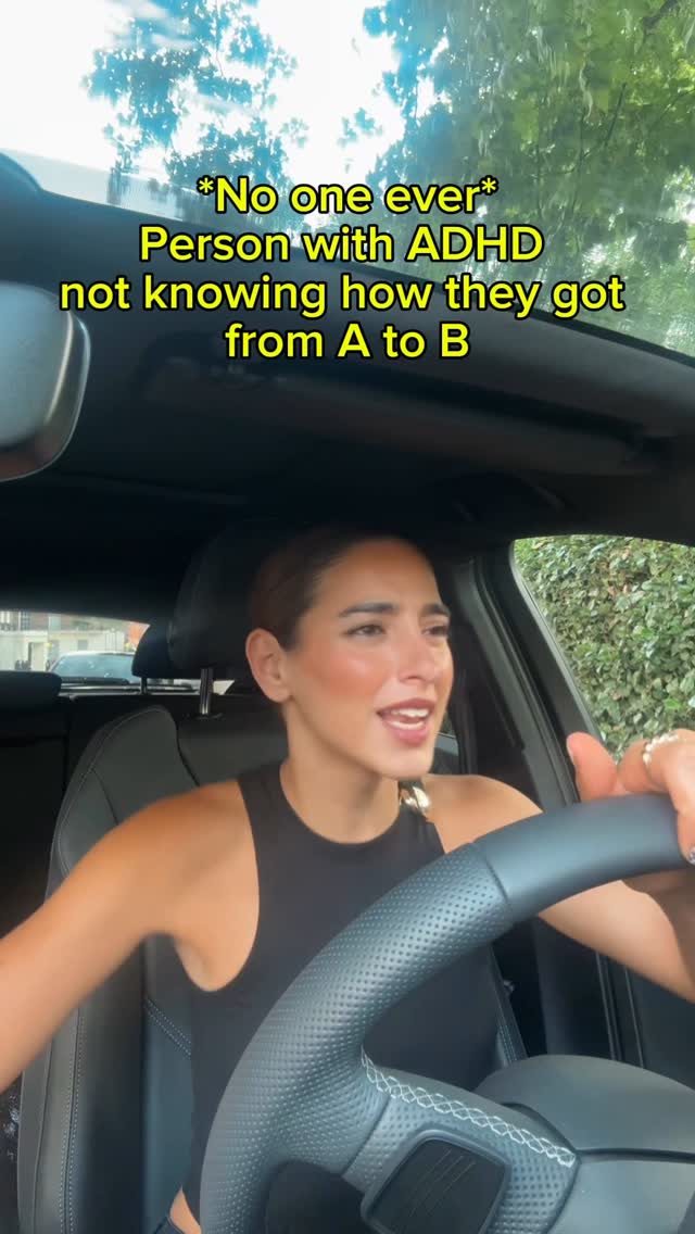 A woman is sitting in a car, smiling and looking slightly to the right while holding the steering wheel. Text overlays say, '*No one ever* Person with ADHD not knowing how they got from A to B'. The background is out of focus, with treetops and a blue sky visible through the windshield.
