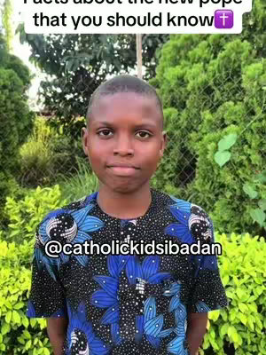 A medium shot features a young Black boy centered, looking directly at the viewer with a neutral expression. He wears a dark blue, black, and white patterned shirt. The background is a wall of green foliage illuminated by sunlight, creating a natural setting.