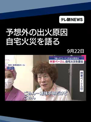 The image is a screen capture from a news broadcast. In the upper left corner, there is a logo that reads "テレ朝NEWS". The main content is a frame of video featuring a man with a distinctive curly hairstyle. He's wearing a checkered shirt and visible in a room setting. Below the video frame, there is overlaid text in Japanese with multiple components including the date. A secondary video frame is slightly visible to the side. Behind the video, the background is dark. Elements across the image include logos, and overlaid text.