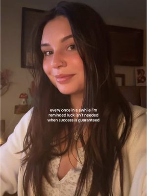 A medium shot of a young woman with long, dark hair. She is smiling slightly and looking at the camera. The background is blurred, but appears to be a cozy indoor setting. Text overlayed at the bottom reads, 'every once in a awhile i'm reminded luck isn't needed when success is guaranteed'.