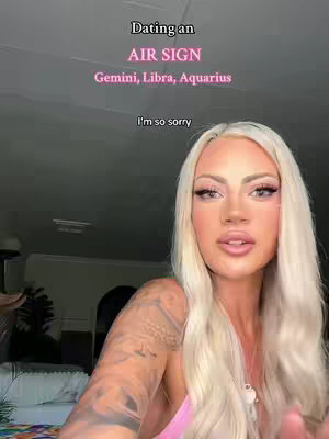 A woman with long blonde hair and full makeup sits in front of a blurry background. Text overlays are at the top, describing the video's topic The woman is wearing a pink top. Her left arm displays a tattoo. The lighting is dim.
