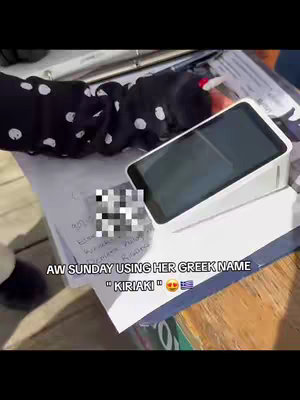 A shot featuring a person's hand and arm in a dotted sleeve, writing on a paper with the name "Kiriaki," a card payment machine and a blurred out note on a table.