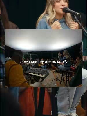 The cover image is a vertical video snapshot. It features a woman, identified as the creator, singing with a microphone in front of a blurred background showcasing a band and audience in a warmly lit setting. The background shows a wide shot of a band setting including a keyboard, guitar and other instruments and people. A superimposed banner at the bottom features the text in white font.