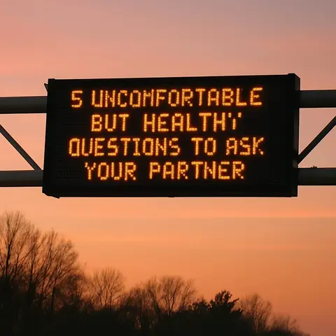 An image of a digital sign displaying the text '5 UNCOMFORTABLE BUT HEALTHY QUESTIONS TO ASK YOUR PARTNER' in orange against a gradient orange and pink sunset background. The sign is mounted above a dark treeline.