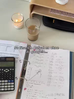 A well-lit desk setup with a lit candle, a glass of coffee, and study materials. A calculator and a binder with handwritten notes are visible, suggesting a study or work environment.