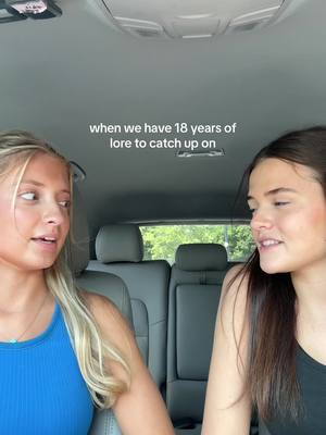 Two young women are seated in the front seats of a car, facing each other. The woman on the left has blonde hair and is wearing a blue top, while the woman on the right has dark hair and is wearing a black top. They are positioned with the car's interior visible behind them, creating a candid and personal atmosphere. Text overlayed on the image reads: 'when we have 18 years of lore to catch up on.'