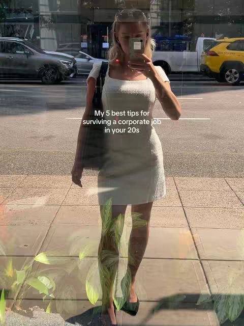 A young woman is taking a selfie in front of a glass window, reflecting a street scene with cars and buildings. She is wearing a white dress and holding a phone, obscuring part of her face. Text overlaid on the image reads "My 5 best tips for surviving a corporate job in your 20s."