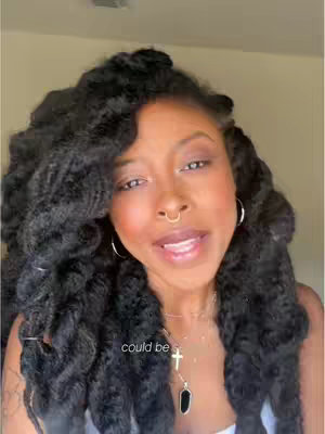 A close-up shot of a woman with dark, curly hair and makeup that includes lip gloss and a nose ring. She is wearing a white top and a necklace with a cross pendant. Overlaid text at the bottom of the screen reads 'could be'. The background is a warm tone.
