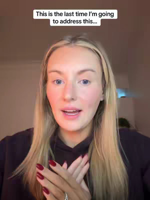 A woman with long blonde hair and a dark colored hoodie is looking directly at the camera with both hands clasped in front of her body. A text overlay is over her head. The background is blurred.