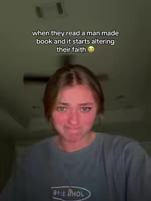 A young woman with short, light brown hair and flushed cheeks is looking at the camera with a concerned expression. Text overlays the top reads "when they read a man made book and it starts altering their faith". The background is a dimly lit room with a ceiling fan partially visible. The woman is wearing a dark t-shirt.