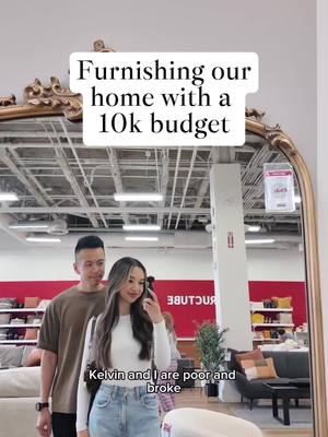 The cover image shows a couple reflected in a large ornate mirror. Text overlays state "Furnishing our home with a 10k budget" and "Kelvin and I are poor and broke". They appear to be in a furniture store, with various displays in the background.