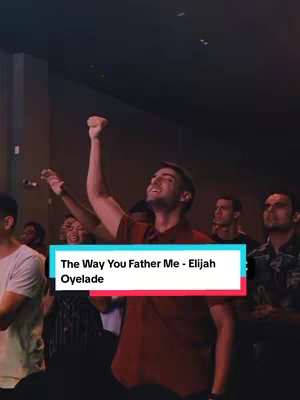 A group of people are gathered, likely in a place of worship. The primary visual element is a man standing with his right arm raised, fist clenched, while looking up towards the ceiling. The background shows several other people with their hands raised as well. Overlayed in the image is a large rectangular box with the text 'The Way You Father Me - Elijah Oyelade'. The colors are muted, with the scene illuminated by warm lighting. The overall composition suggests a moment of passionate worship or performance.