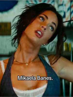 A close-up shot features a woman with dark hair looking up with an opened mouth. She is wearing a necklace and a sleeveless top over a white top. Text overlayed on the image reads "Mikaela Banes."