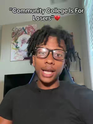 A young man with dark hair and glasses is centered in the frame, speaking directly to the camera. Above him, text reads "Community College Is For Losers" with a red heart emoji. The background is an interior space, with an abstract painting visible.