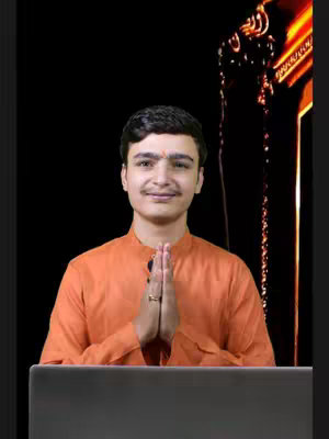 A young man in an orange garment, hands clasped in a gesture of greeting, sits before a laptop. The backdrop is a blurred, dark space with golden light streaks to the right. The overall composition is warm and inviting.