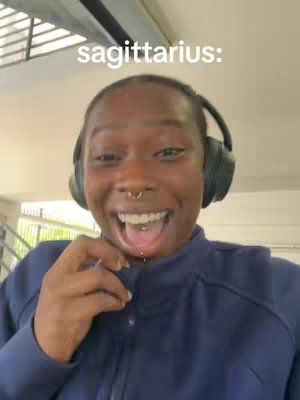 A close-up shot of a person with dark skin, wearing headphones, and smiling widely with their mouth open, tongue piercing visible. The background is indistinct, with glimpses of a ceiling or overhang, and there is the overlaid text in the top of the picture.