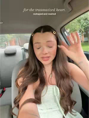 A woman sitting in a car, looking towards the camera and talking. The text overlay appears at the top of the frame, and various elements of the car's interior, like the seat and window, are visible in the background.