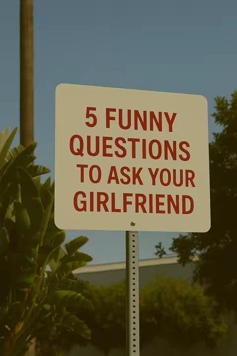 A photograph captures a sign against a backdrop of foliage and sky. The sign is rectangular with rounded corners, painted cream. The text, in a bold, red, sans-serif font, reads: '5 FUNNY QUESTIONS TO ASK YOUR GIRLFRIEND.' The font size increases as the phrase gets longer to fill each line. The background is filled with a mix of green foliage and a clear blue sky. The composition is straightforward, with the sign centrally positioned and well-lit.