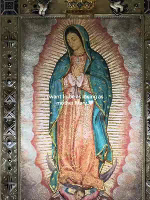 The image is an artistic representation of the Virgin Mary. She is depicted from the chest up, wearing a blue cloak over a peach-colored gown and a veil. She has her hands clasped in prayer, and her gaze is directed downwards. She is surrounded by an ornate frame and a halo of gold radiating light. The words 'I want to be as loving as mother Mary' are written in a white font at the bottom half of the image.