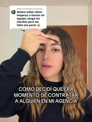 The cover image features a woman holding a makeup brush near her eyebrow while looking directly at the camera. Overlayed text in a bold, white font states, "CÓMO DECIDÍ QUE ERA MOMENTO DE CONTRATAR A ALGUIEN EN MI AGENCIA". A comment bubble in the top left corner contains text. The background is a simple interior space. The woman is wearing a dark long-sleeved shirt and has long wavy hair. The lighting seems natural.