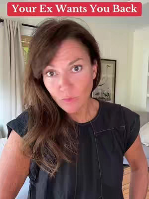 A woman with dark hair and a black top looks directly at the camera with a subdued expression. The background includes curtains and a framed picture.