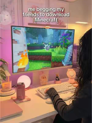 A person is sitting at their gaming setup, which includes a large monitor displaying a Minecraft scene, a white keyboard, and several pink accessories. Text overlays on the image, showing the message.