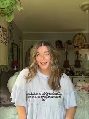 A young woman with long, wavy brown hair stands facing the camera in a bedroom. She wears a light blue top and smiles. Text overlays the image.