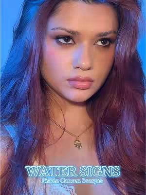A close-up of a person with long, wavy, reddish-purple hair. The person has fair skin, a slight smile, and is wearing makeup. The background is lit with blue and purple hues. The text overlay reads "WATER SIGNS Pisces, Cancer, Scorpio."