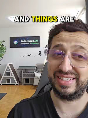 A man with glasses smiles at the camera in a room with a sign on the wall.