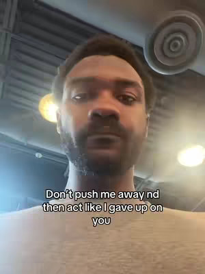 A selfie-style video cover image featuring a Black man in a close-up shot. He has a groomed beard and appears to be indoors, possibly in a public space, with overhead lighting visible. Text overlayed over the man’s face conveys a message regarding relationship dynamics and emotional distance.