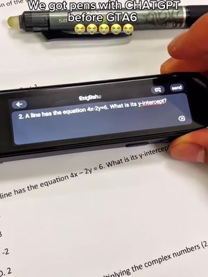 The image features a close-up of a hand holding a black scanning pen over a sheet of paper with a printed math problem. A digital display on the pen shows a math question in English and includes the question which appears to be about y-intercepts. Above the pen, there is a black pen and an eraser. The background is white with faint printed text related to complex numbers.